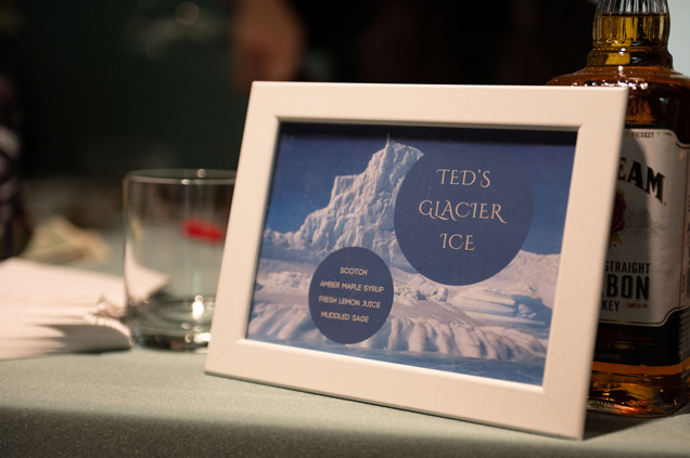 A sign that states 'Ted's Glacier Ice' leaning on a bottle of alchohol. 